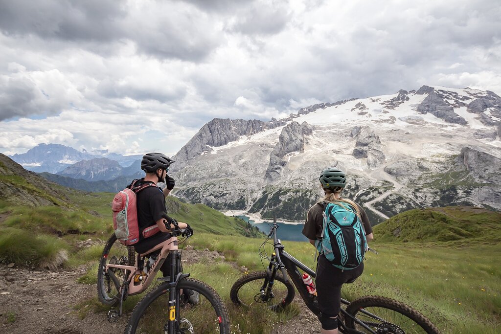 Persone che vanno in bike di fronte al Lago di Fedaia e la Marmolada in Val di Fassa