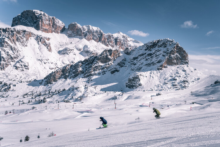 Coppia di amici scia sulle piste della skiarea Belvedere di Canazei. Sullo sfondo Sass Becé e Sass Pordoi | © Patricia Ramirez  - Archivio immagini ApT Val di Fassa